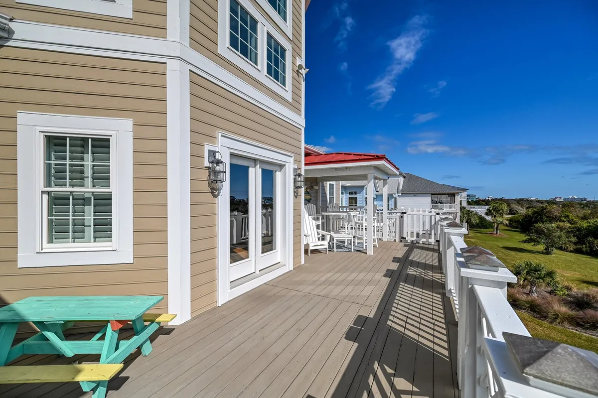 The image presents a cheerful exterior deck with a colorful picnic table, surrounded by lush greenery and large windows connecting indoors and outdoors. The space is inviting for both people and pets, with ample room for resting and enjoying the fresh air.