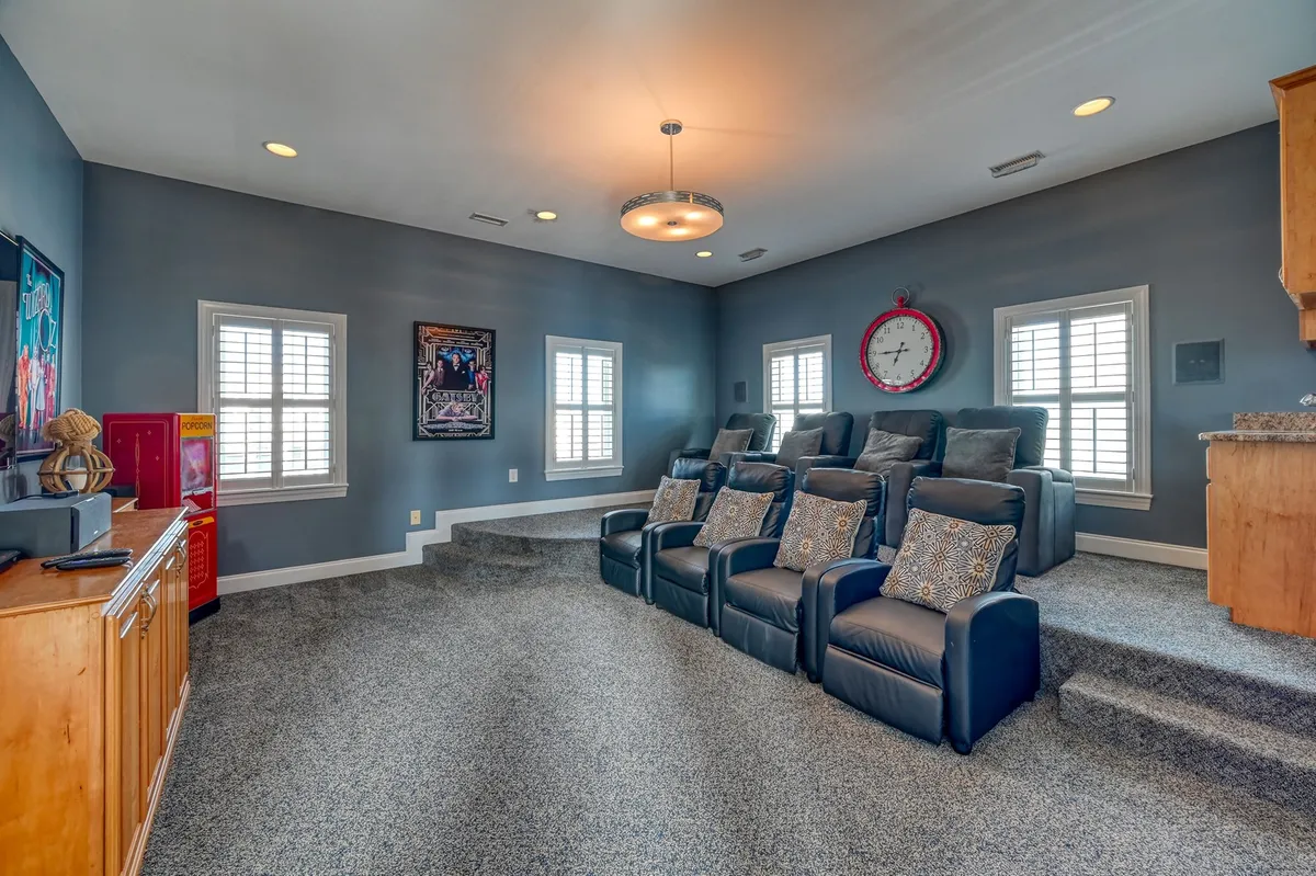 A dedicated home theater room with plush, tiered recliner seating, wall art, a bar area for refreshments, and a large clock. The setup is ideal for immersive movie nights or lively game nights with family and friends.