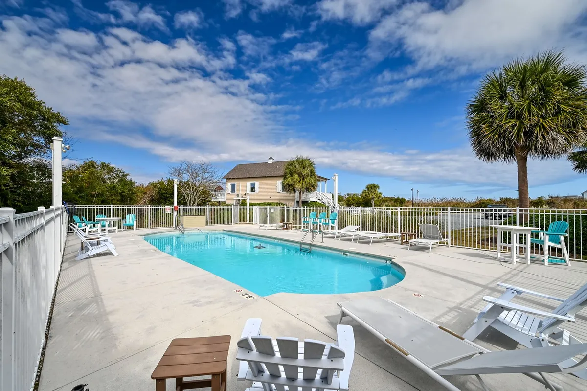 A sun-drenched swimming pool lined with inviting lounge chairs and framed by palm trees. The sparkling water glimmers in the sunlight, while the tranquil poolside area offers ample space for relaxing, sunbathing, or socializing with friends and family.