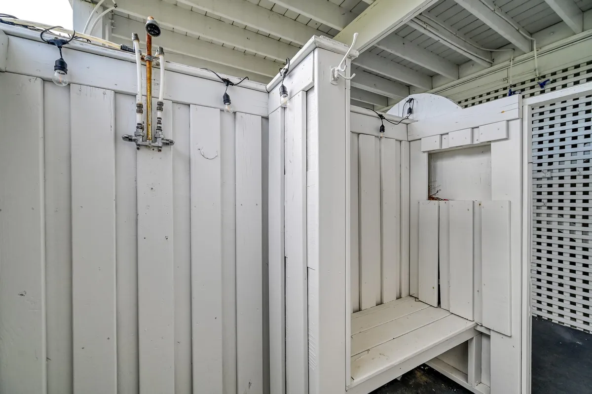 This image shows an outdoor shower area featuring wooden panels and overhead lighting, evoking a casual, beachside feel. The design is practical for washing off after beach outings, and the setting is both refreshing and accessible.