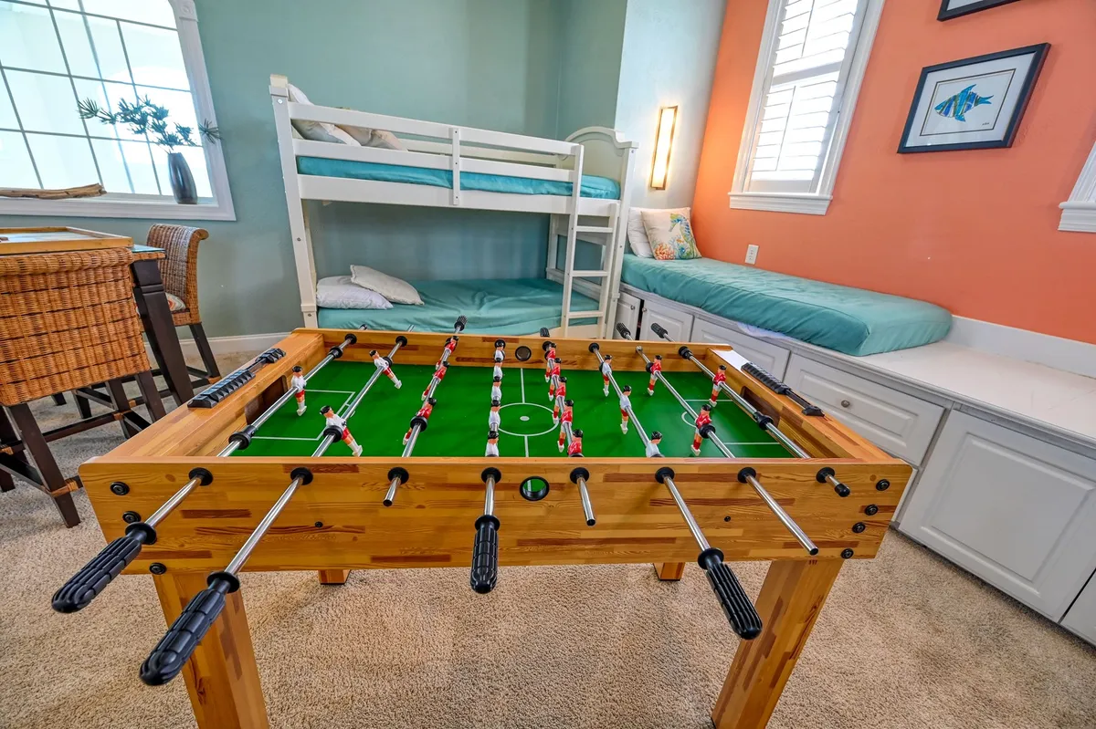 This image captures a lively interior featuring a foosball table, bunk beds, and playful wall art. The room is clearly designed for group games and sleepovers, evoking a sense of youthful energy and camaraderie.