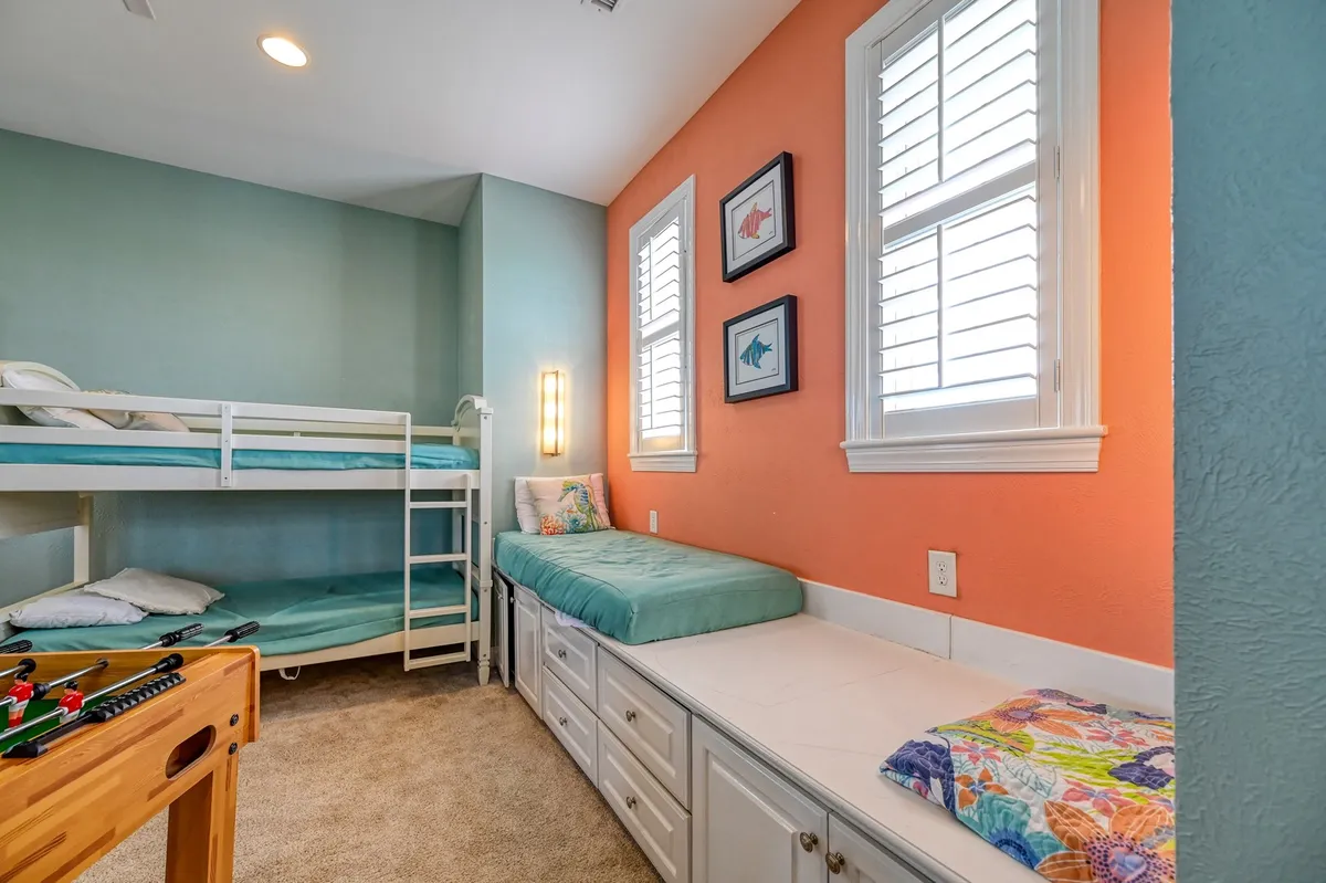 A cheerful, relaxed space featuring bunk beds, a reading nook with colorful cushions, and a foosball table in the background. The ambiance is playful and inviting, ideal for group relaxation and late-night fun.