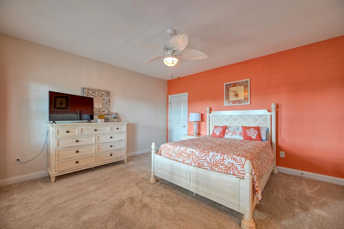 A sunlit bedroom featuring a bed with coral-patterned bedding, a white dresser, and elegant wall art. The room feels fresh and comfortable, with natural light streaming in to enhance the sense of calm and privacy.