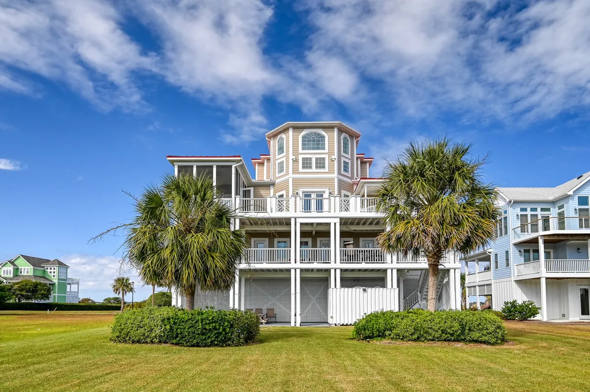 The image showcases a spacious, multi-story beach house surrounded by swaying palm trees, with an inviting open grassy area in the foreground. The setting exudes a welcoming, cheerful atmosphere perfect for family gatherings or relaxing outdoors, and hints at scenic sunset views from the balconies and tranquil moments on the porch.