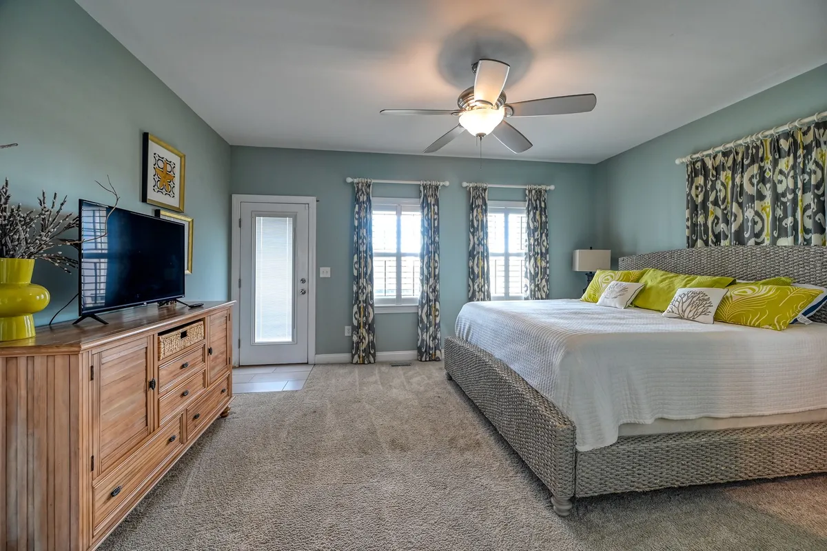 A spacious bedroom featuring a large bed adorned with decorative pillows, a wooden dresser, and a television. The room's neutral palette and plush bedding create an inviting, restful atmosphere ideal for unwinding after a day in the sun.