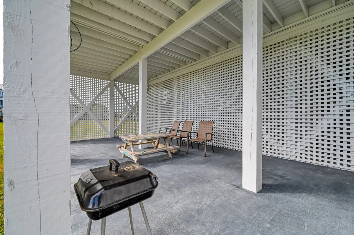A shaded patio area with a grill, wooden picnic table, and lounge chairs, set up for outdoor dining or casual gatherings. The space is ideal for barbecuing, sunset dinners, and celebrating with loved ones in a comfortable and scenic setting.